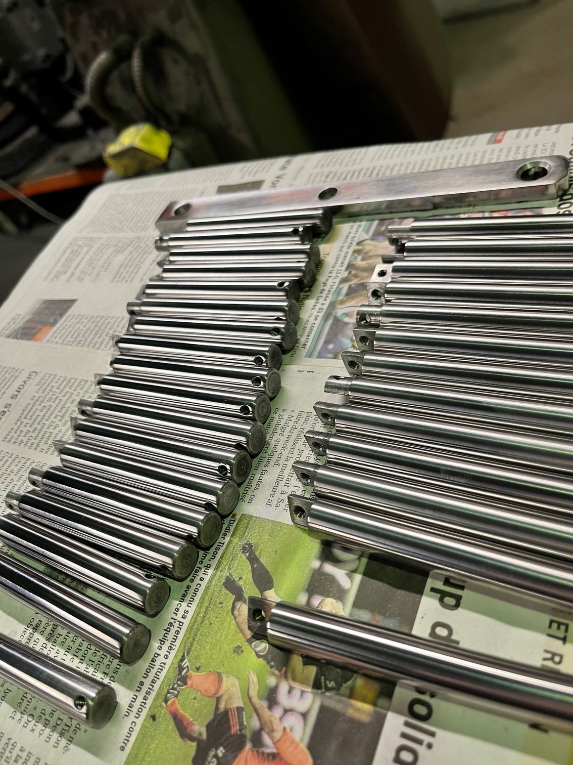 Des rangées de tiges et de plaques métalliques brillantes sur du papier journal.