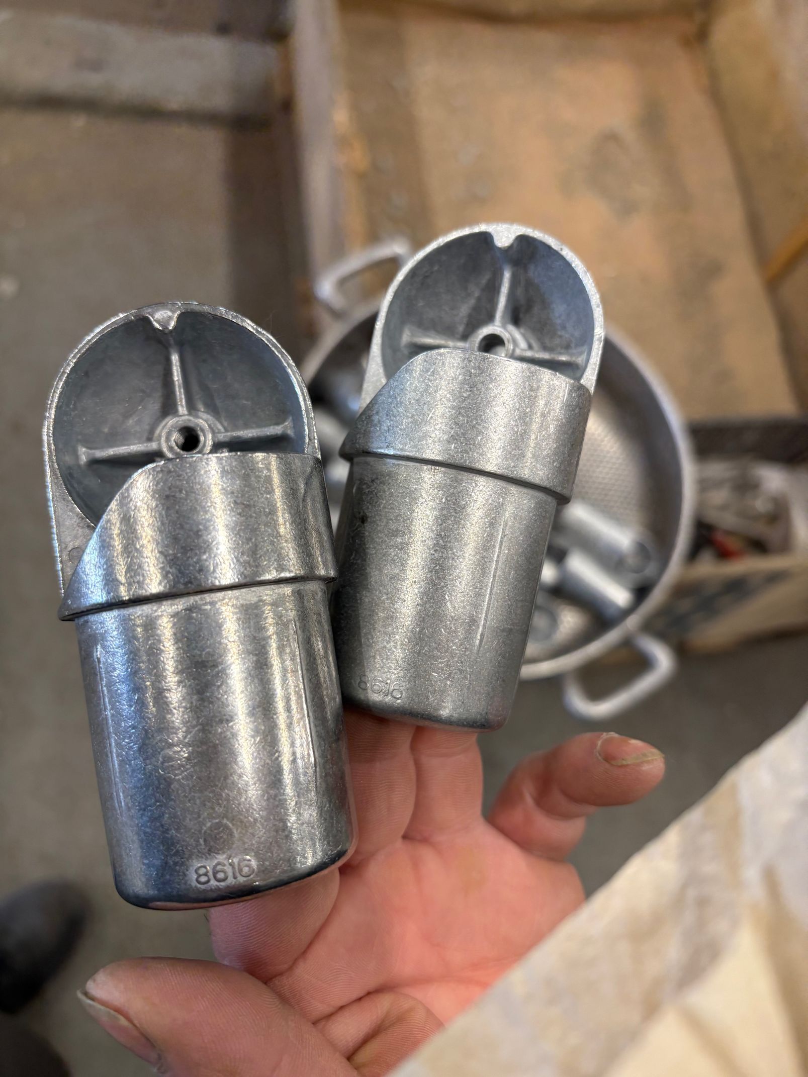 Deux embouts de pieds de chaise en métal argenté sont tenus à la main. D'autres se trouvent dans un récipient métallique.