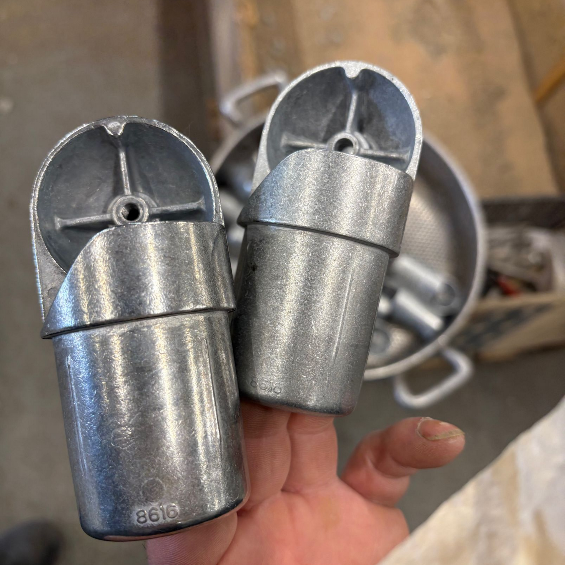 Deux embouts de rambarde en métal coulé, tenus à la main, avec un plat peu profond contenant des pièces similaires en arrière-plan.