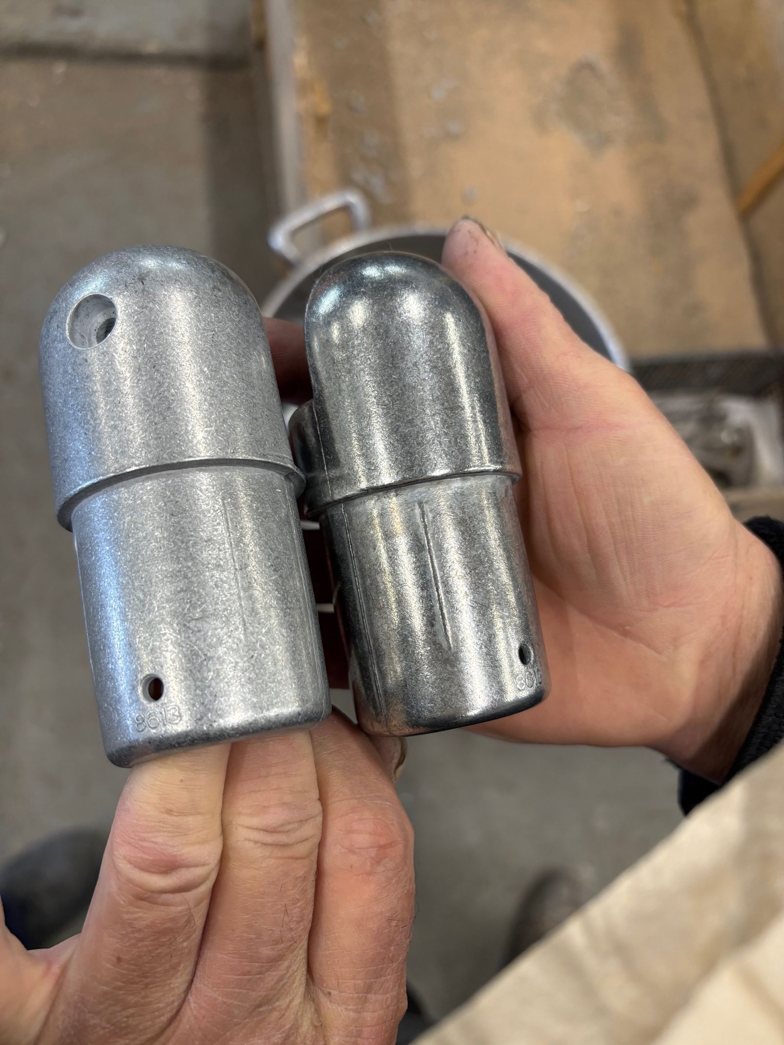 Deux pièces métalliques cylindriques, tenues une dans chaque main, présentant un sommet bombé et de petits trous.