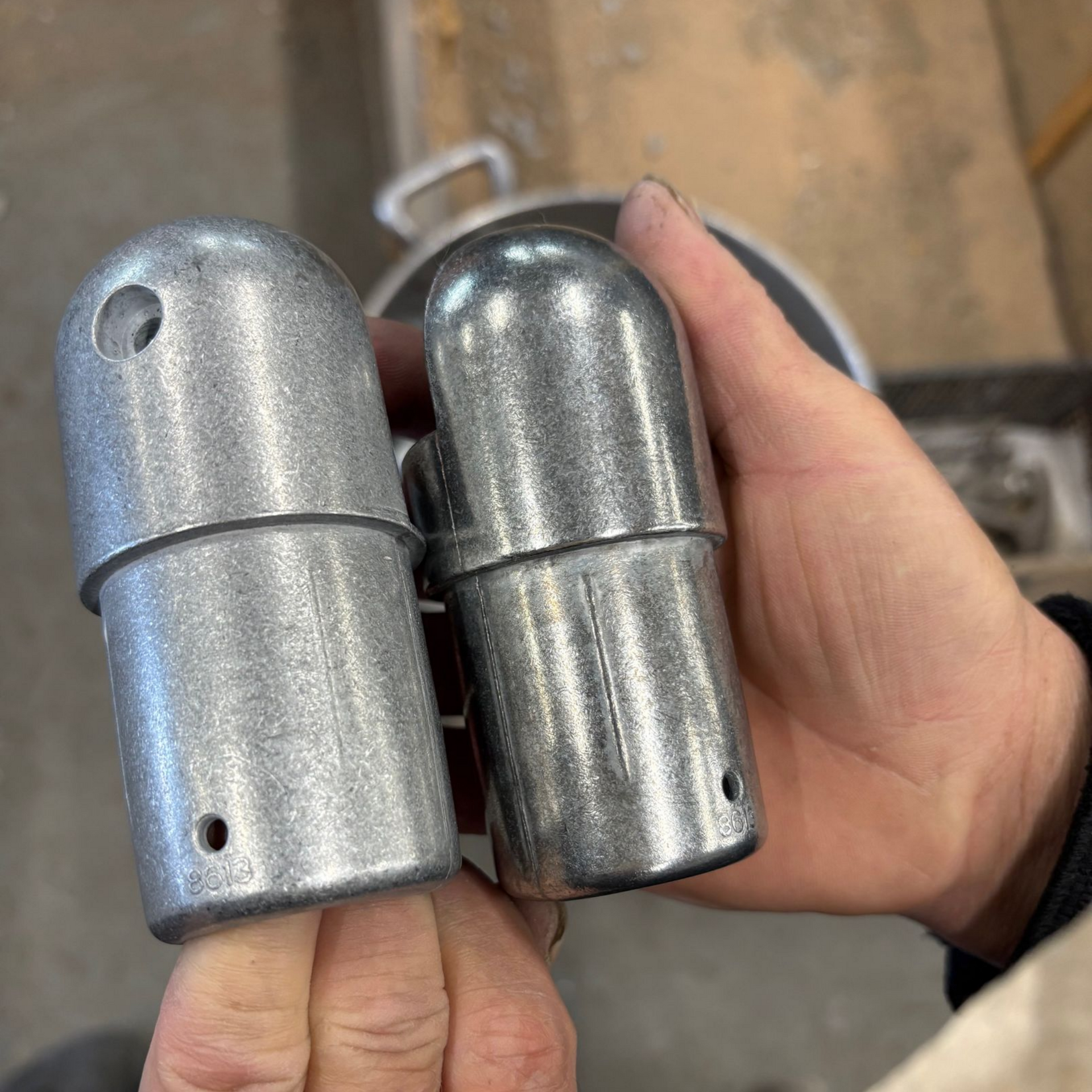 Deux raccords de tuyauterie en métal argenté tenus à la main, l'un d'eux étant percé d'un trou.