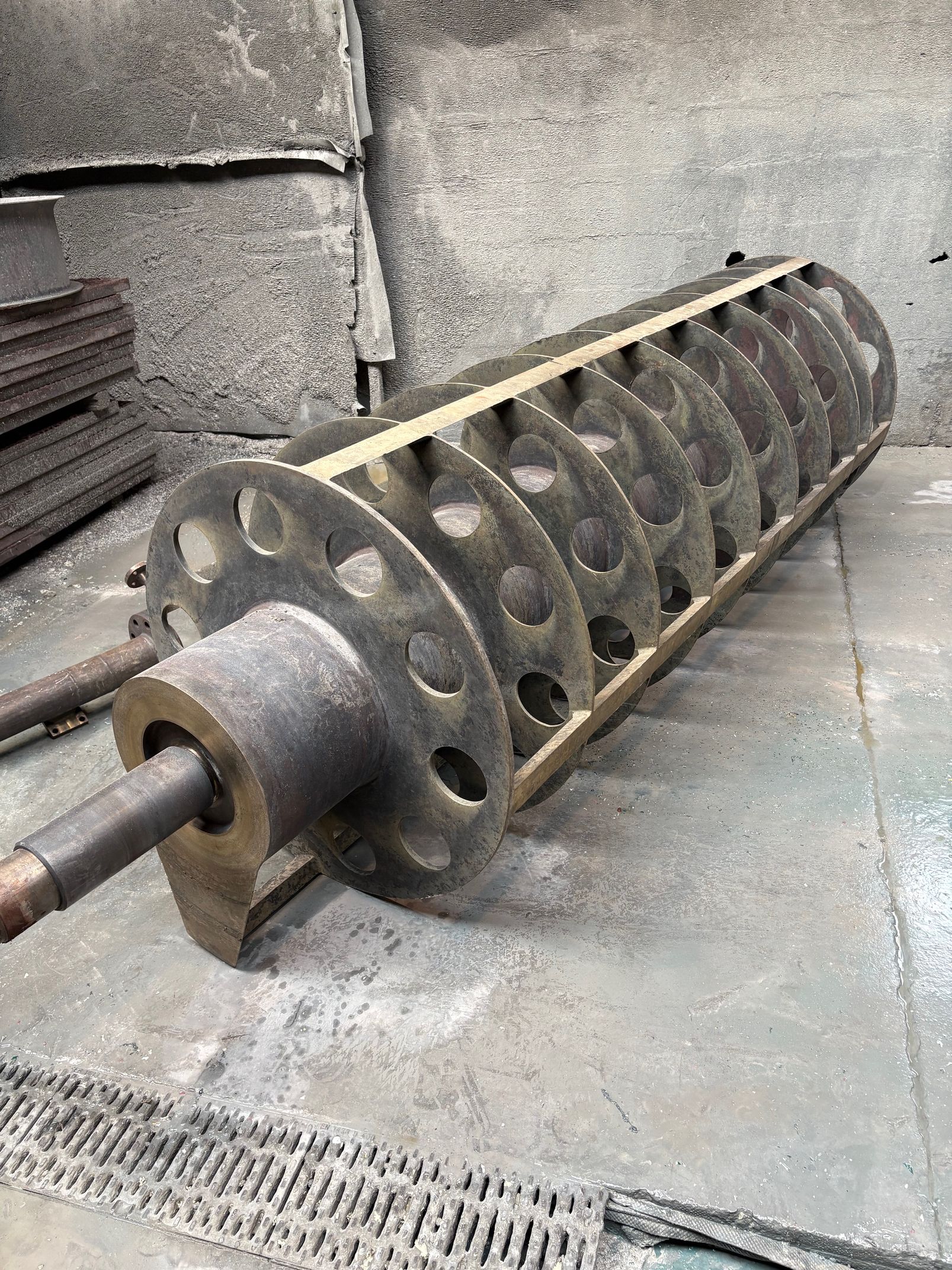 Un long tambour cylindrique métallique muni de plaques circulaires perforées, posé sur le sol d'un atelier.