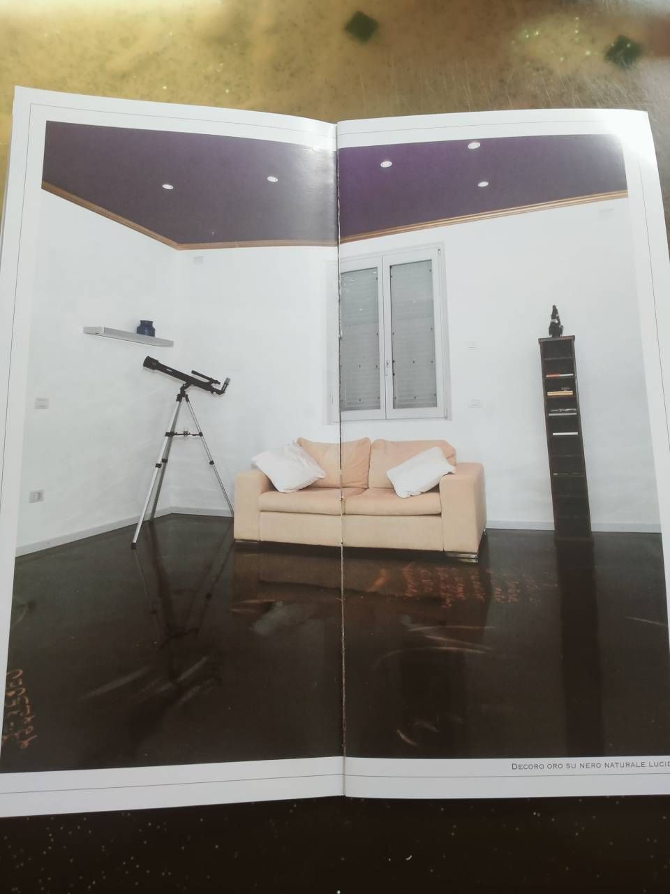 Soggiorno con divano beige, telescopio su treppiede, parete bianca, pavimento scuro lucido e alta mensola nera.