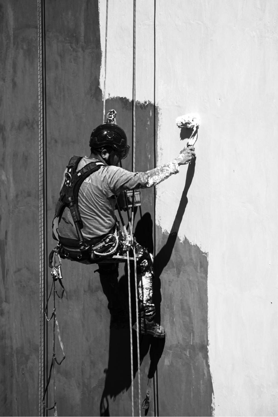 Un operaio dipinge un grande muro, sospeso con delle funi in un'imbracatura.