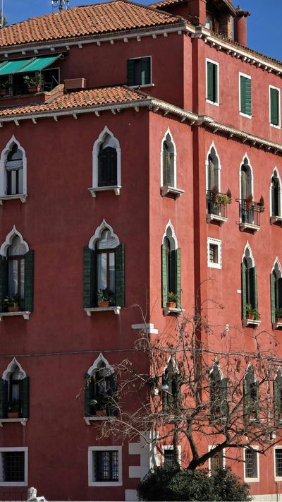 Edificio in stucco rosso con finestre ad arco e tetto in terracotta, visto di profilo contro un cielo azzurro.