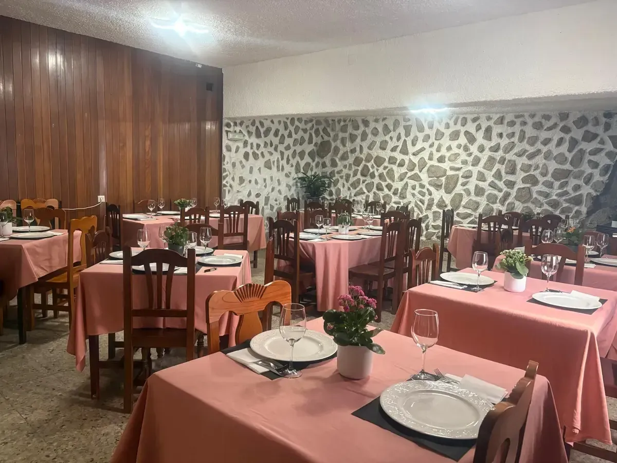 Comedor de restaurante con mesas preparadas para los invitados; manteles rosas, decoración de paredes en piedra y madera.