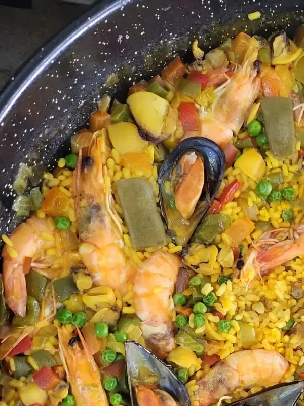Persona sosteniendo un plato de camarones con limón; otros mariscos en el fondo.