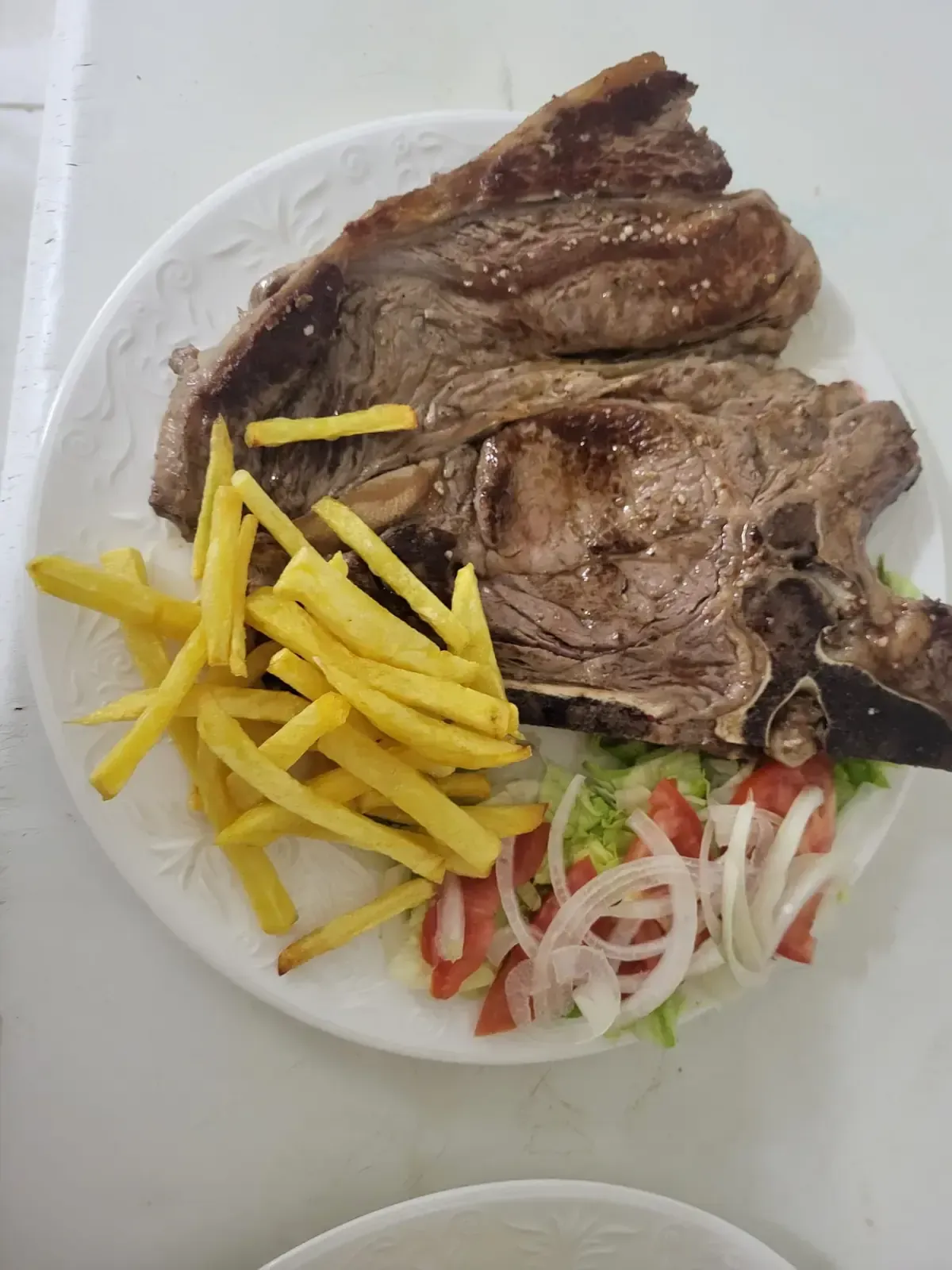 Bistec con patatas fritas y ensalada en un plato blanco.