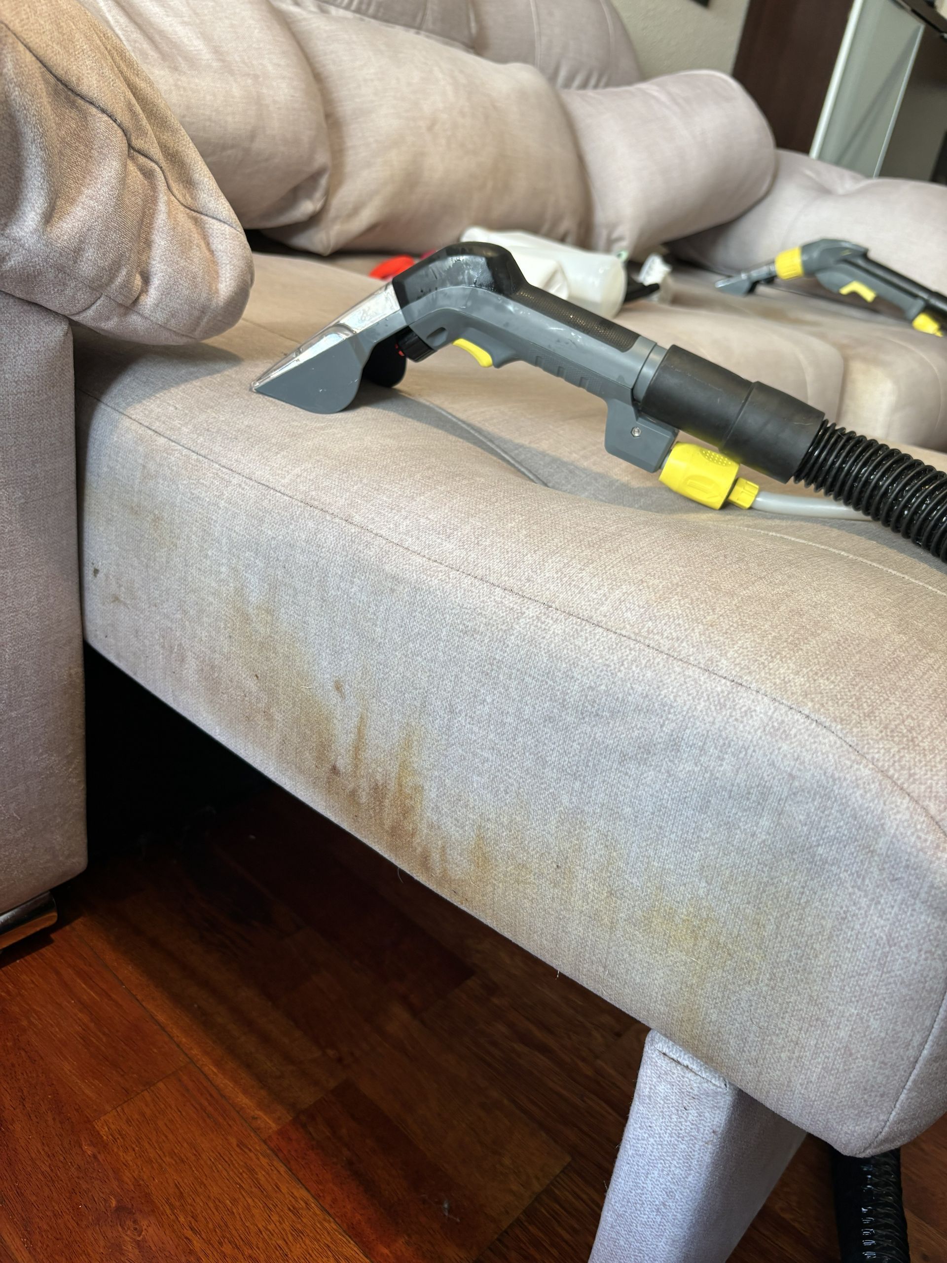 Boquilla de aspiradora debajo de un sofá beige sobre un piso de madera.