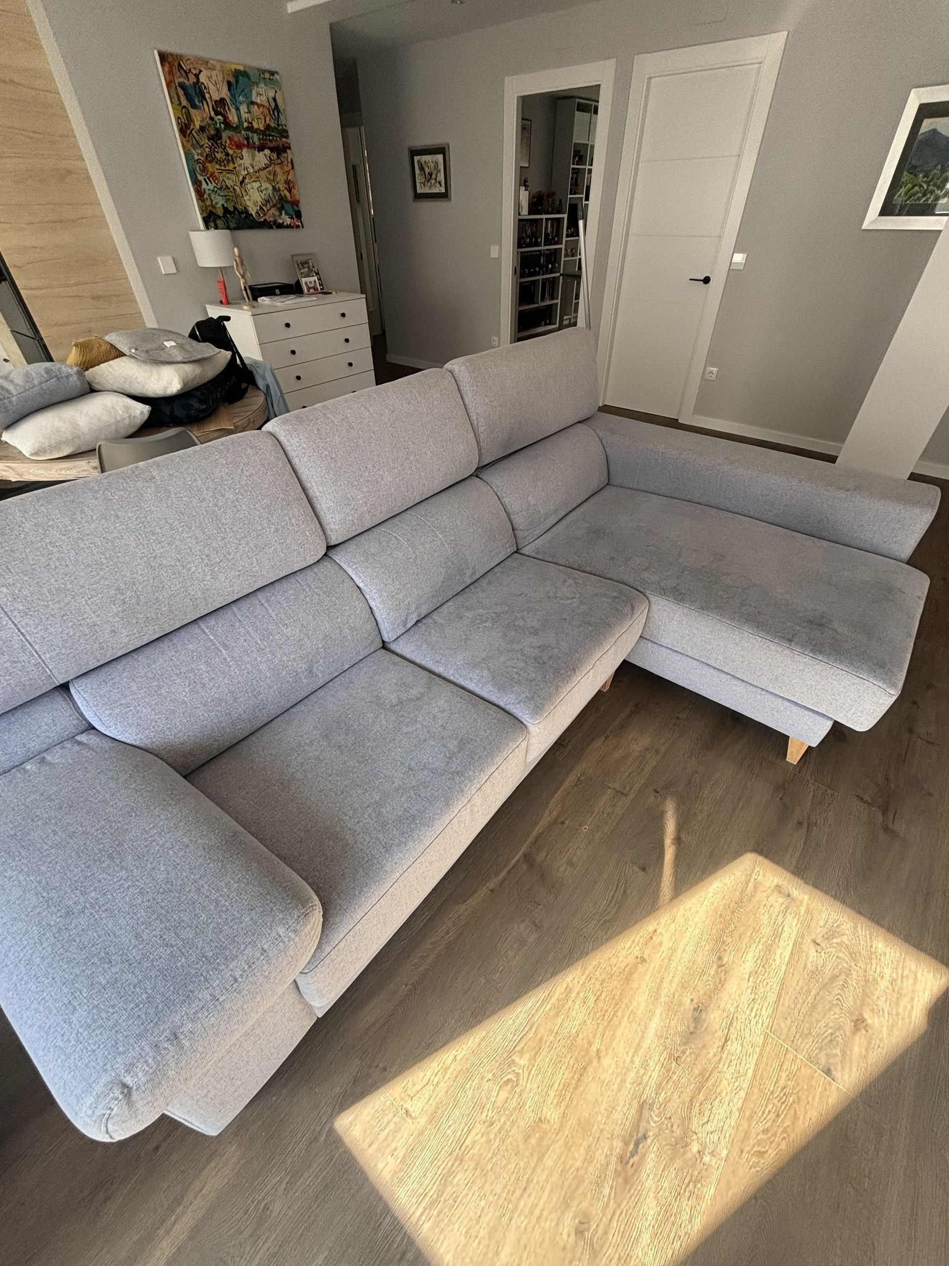 Sofá modular gris en una sala de estar luminosa con luz solar que incide sobre el suelo de madera.