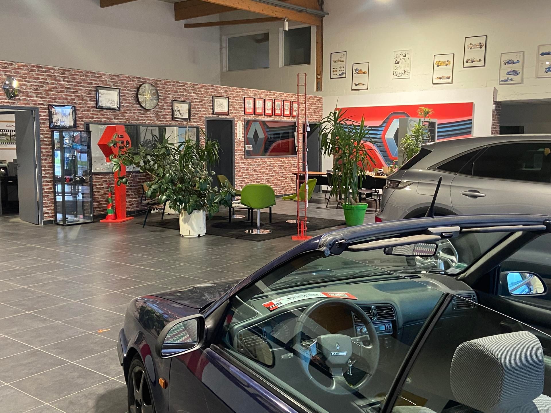 L'intérieur d'une salle d'exposition automobile avec un cabriolet au premier plan et une zone d'attente avec des œuvres d'art sur le mur.