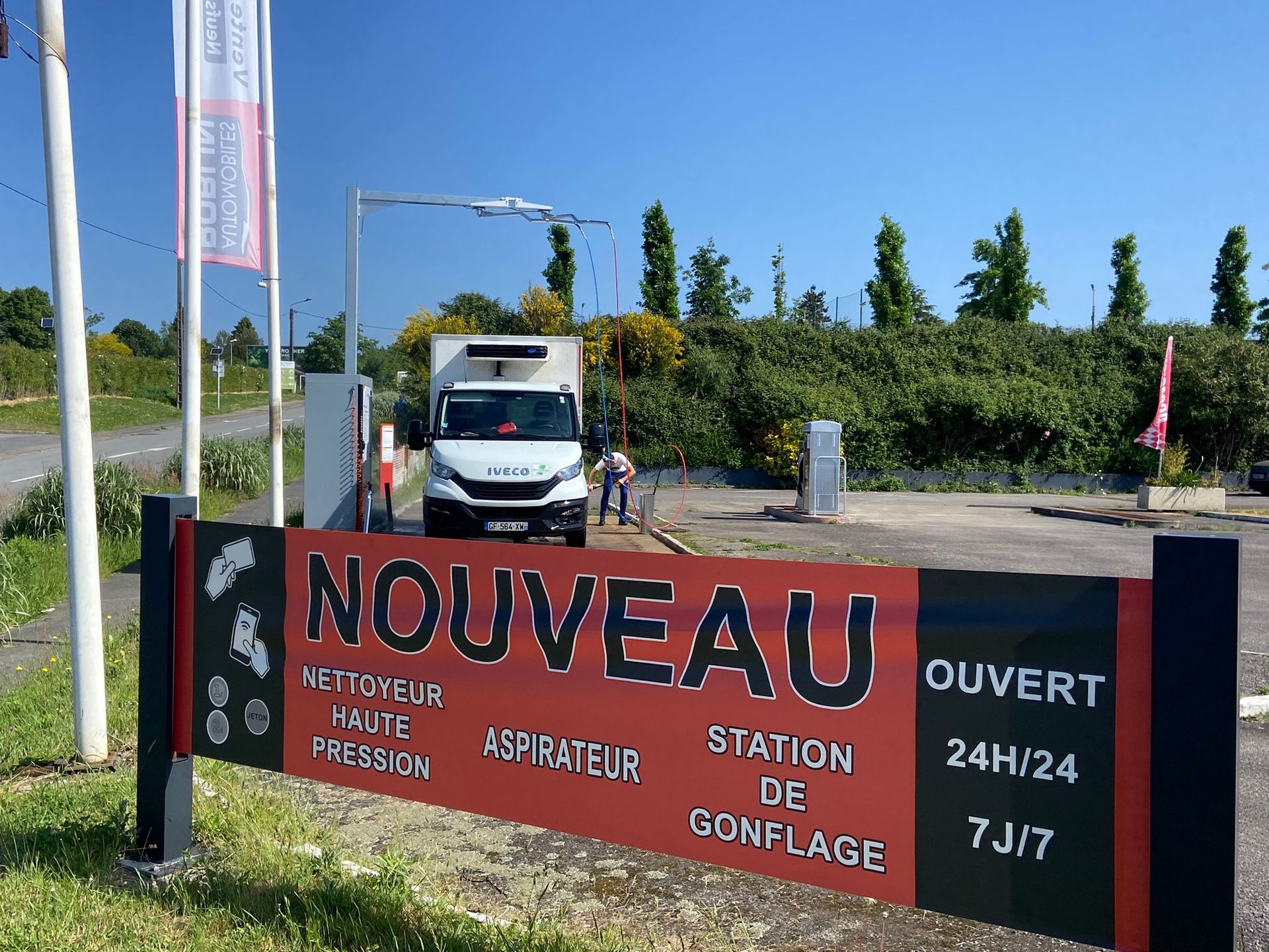 Une personne lave une voiture bleue avec un nettoyeur haute pression dans une station de lavage.