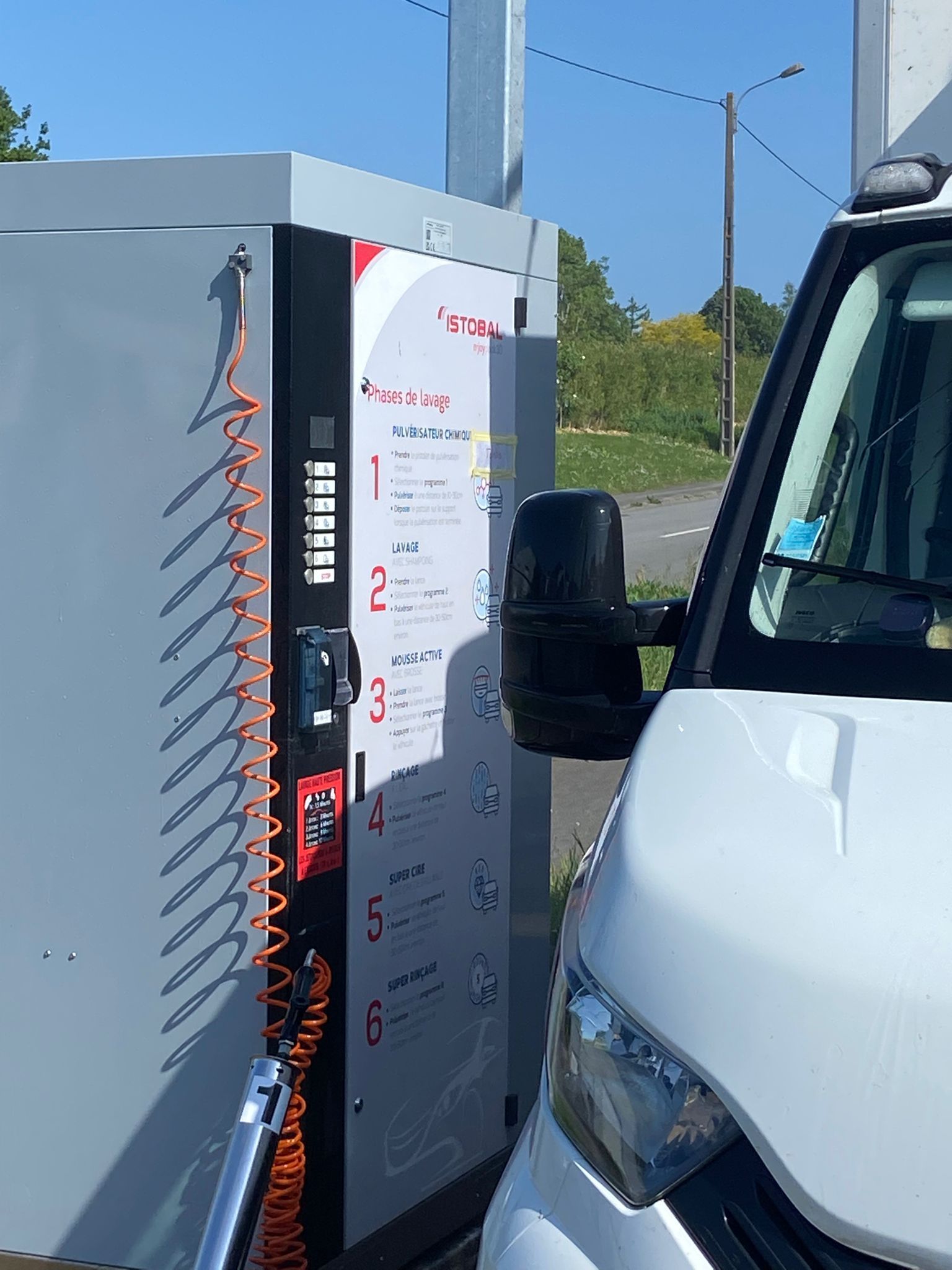 Extérieur d'un concessionnaire automobile, avec une pompe à essence et une signalisation.