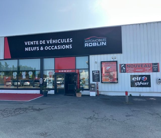 Extérieur du concessionnaire Renault avec des voitures exposées ; voitures bleues, rouges et blanches garées à l'extérieur du bâtiment sous un ciel nuageux.