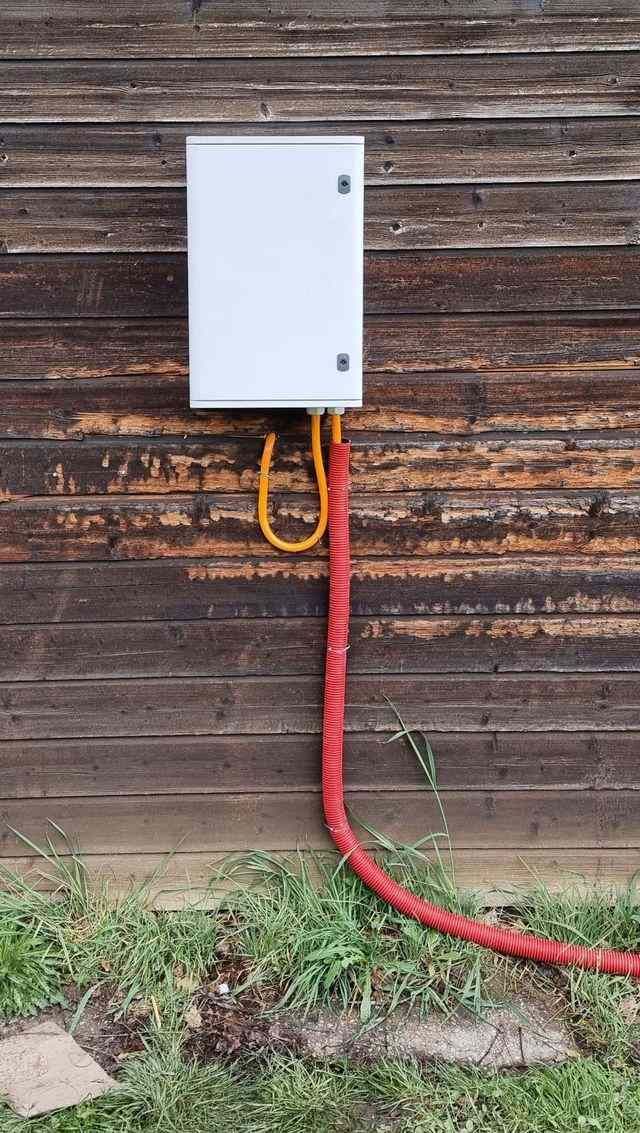 Un tuyau rouge est connecté à une boîte blanche sur un mur en bois.
