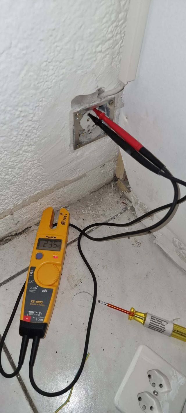 Un voltmètre est branché sur un mur à côté d'une prise.