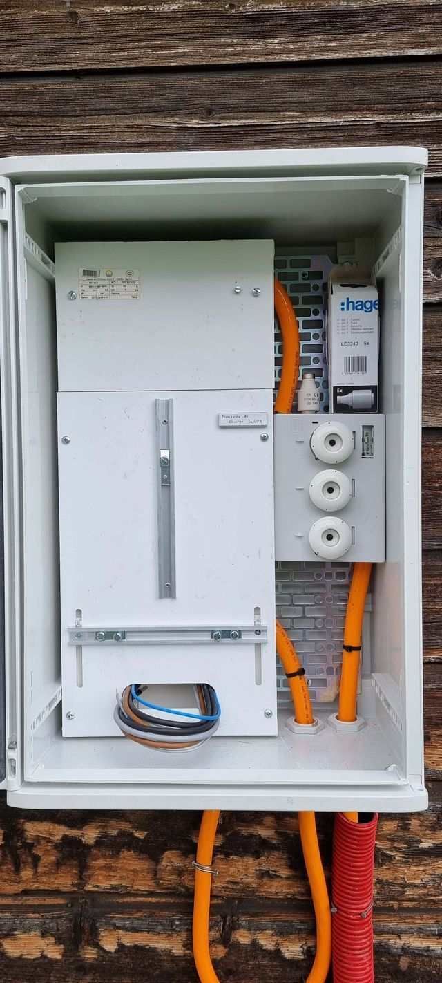 Une boîte blanche avec un tas de fils qui en sortent est posée sur un mur en bois.