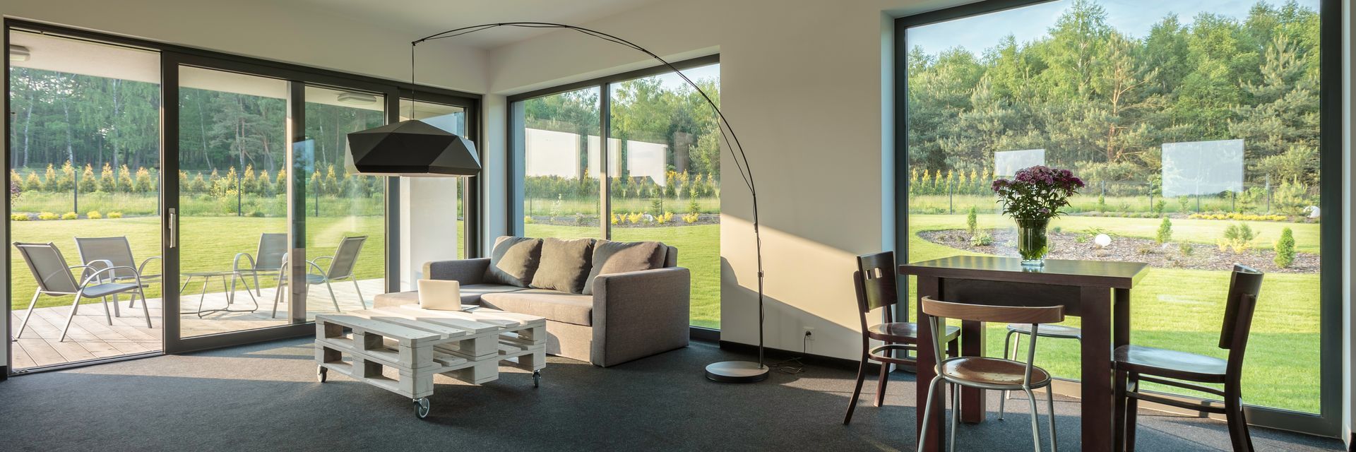 Intérieur d'une maison moderne avec de grandes fenêtres donnant sur un jardin verdoyant et arboré.