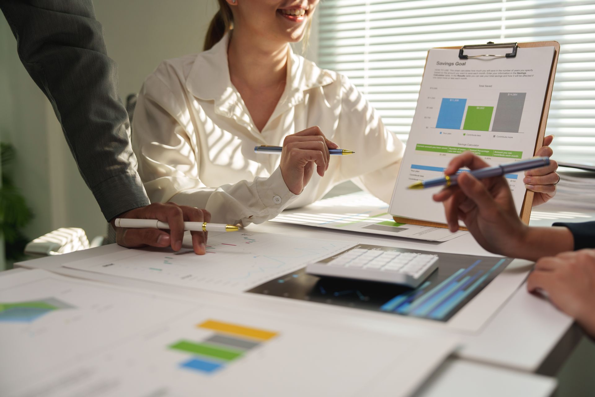 Trois personnes examinent des tableaux et des graphiques à un bureau ; la lumière du soleil entre par une fenêtre.