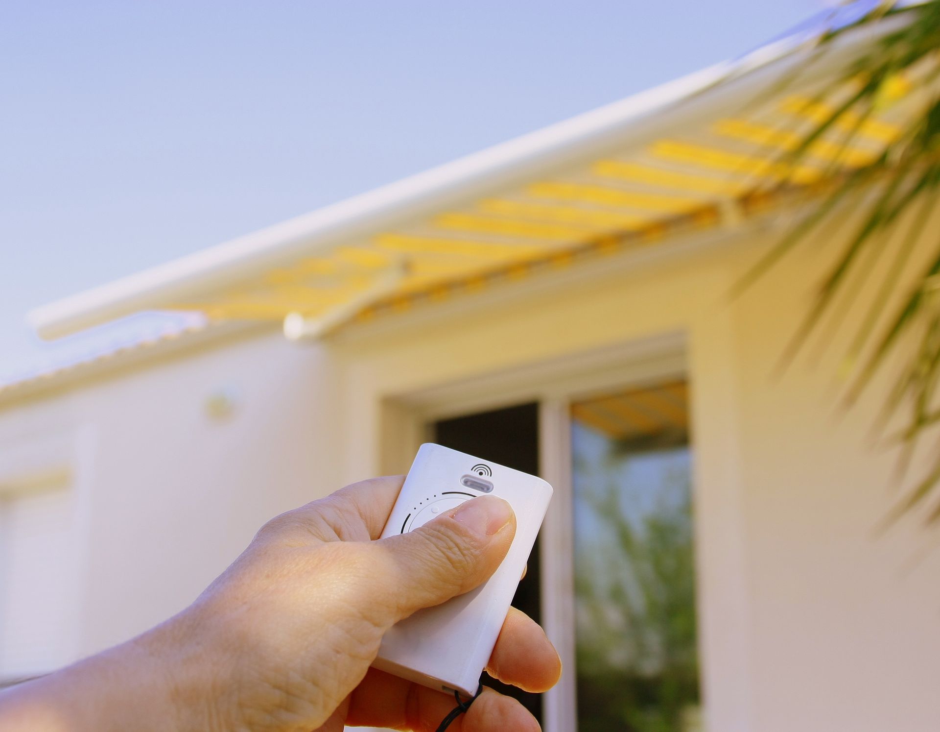 Main tenant une télécommande actionnant un store sur un bâtiment. Ciel bleu.