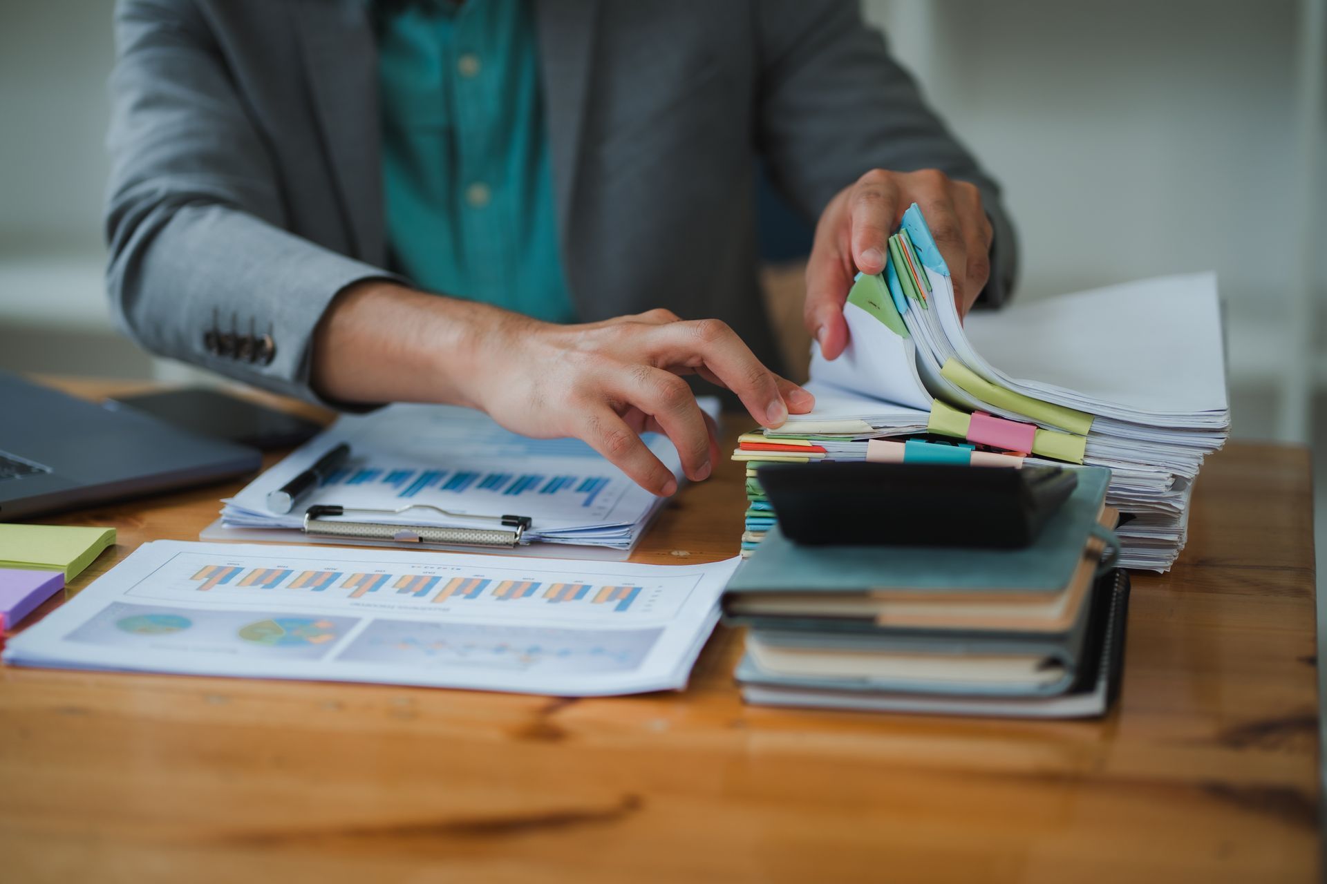 Personne triant des papiers à un bureau avec des graphiques, une calculatrice et un ordinateur portable.