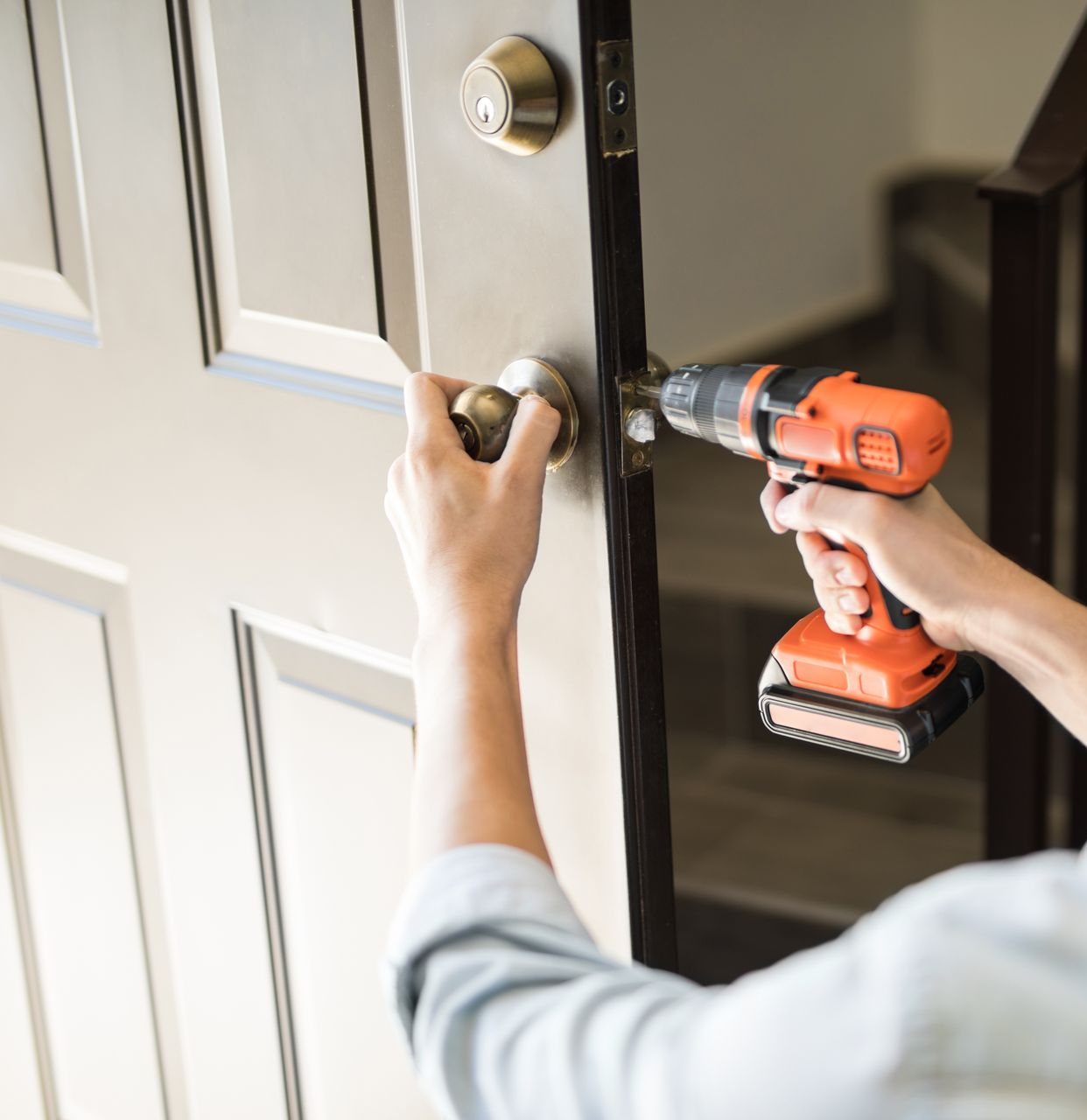 Une personne utilise une perceuse pour installer une poignée de porte sur une porte claire. 