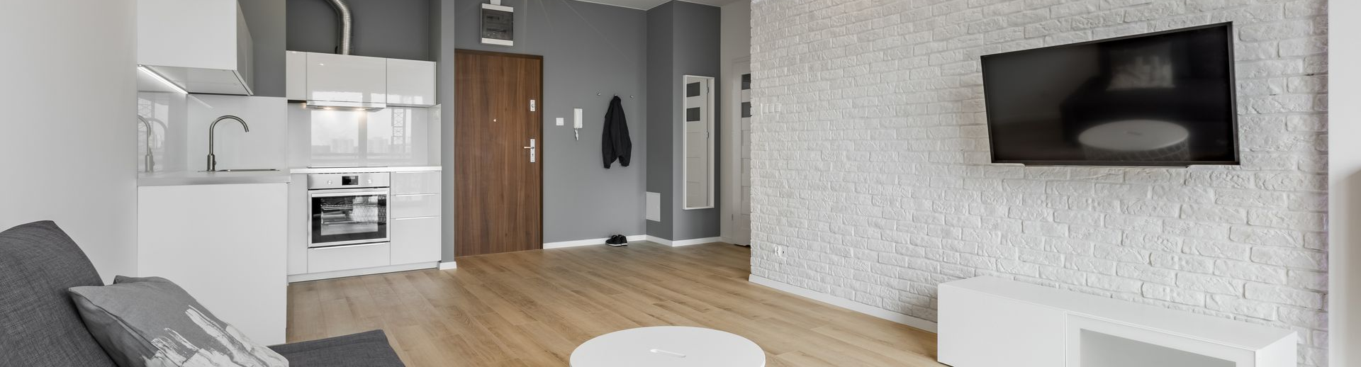 Studio moderne avec cuisine, coin salon avec télévision sur mur texturé et parquet.