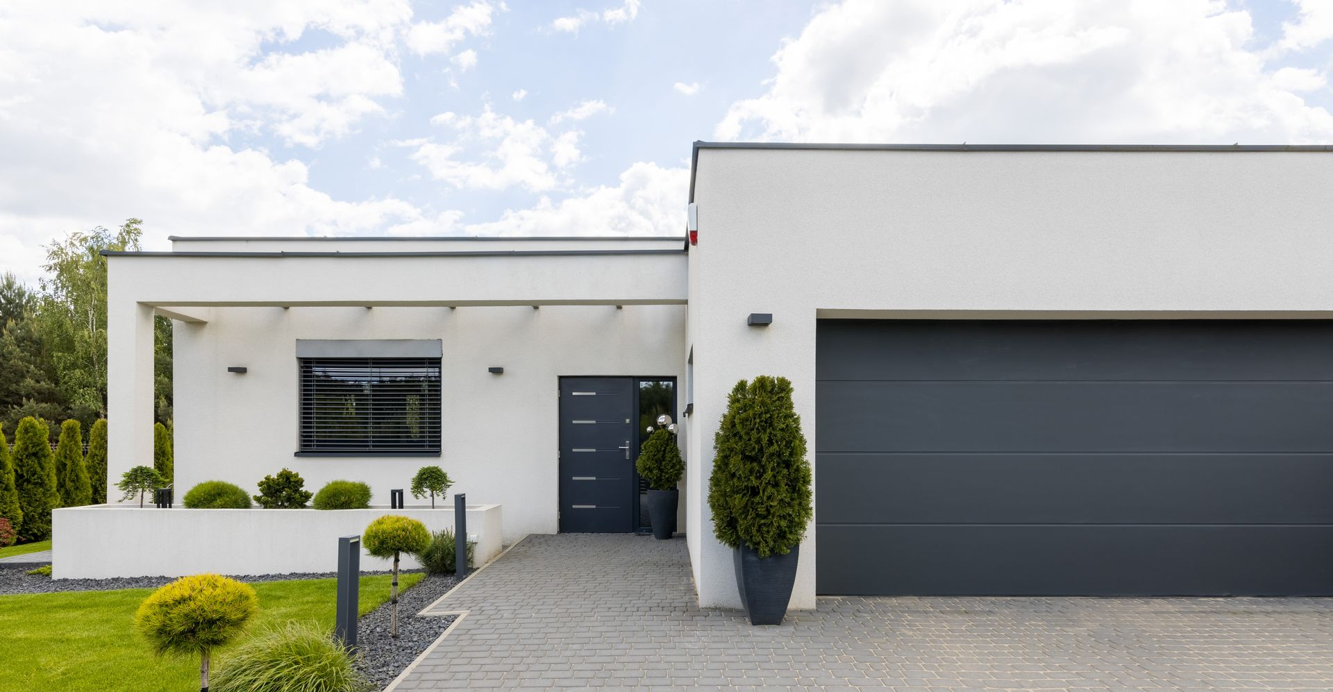 Maison blanche moderne avec porte de garage grise, porte d'entrée et allée ; aménagement paysager à l'avant.
