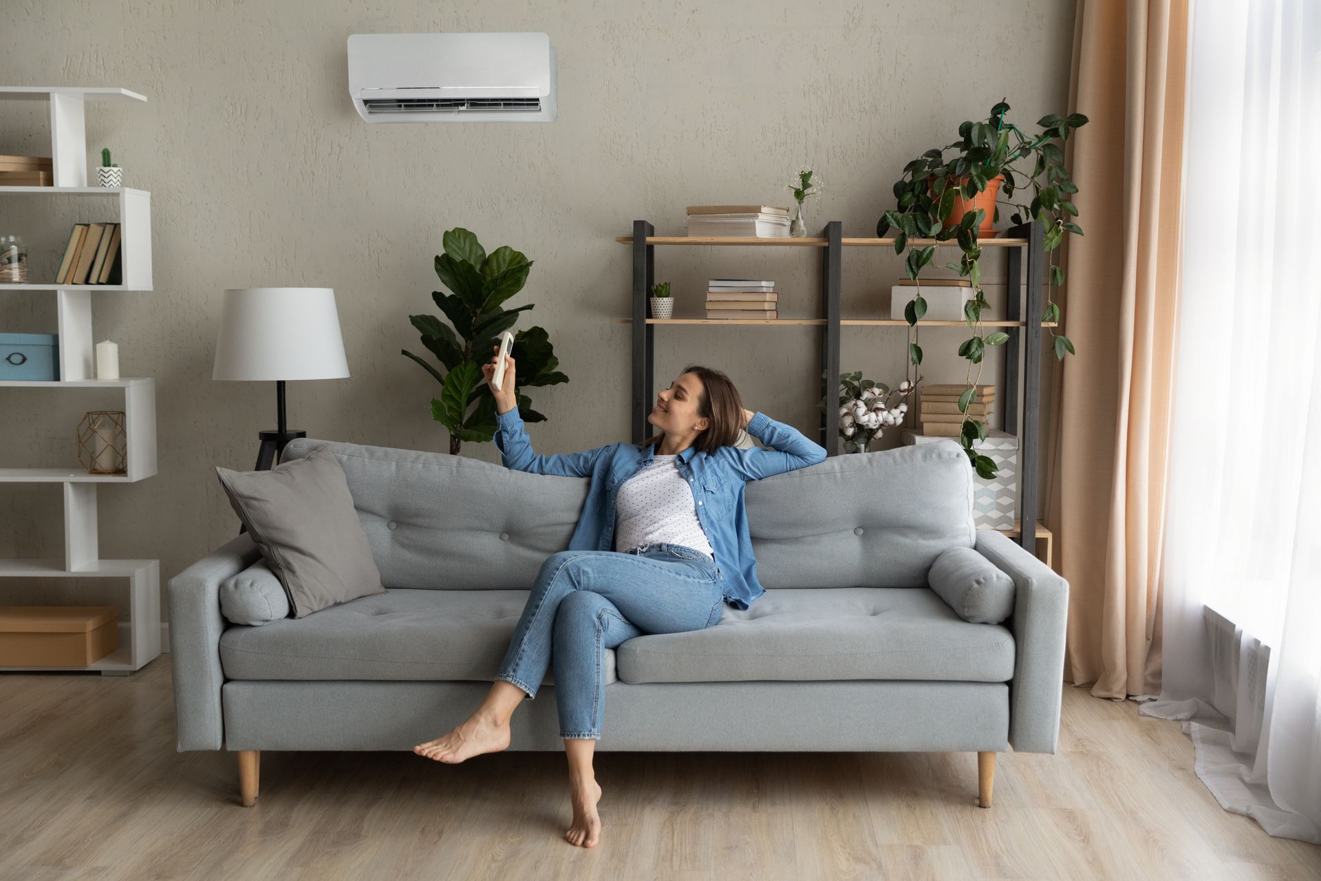 Une femme assise sur un canapé utilise une télécommande, regardant le climatiseur mural dans un salon.