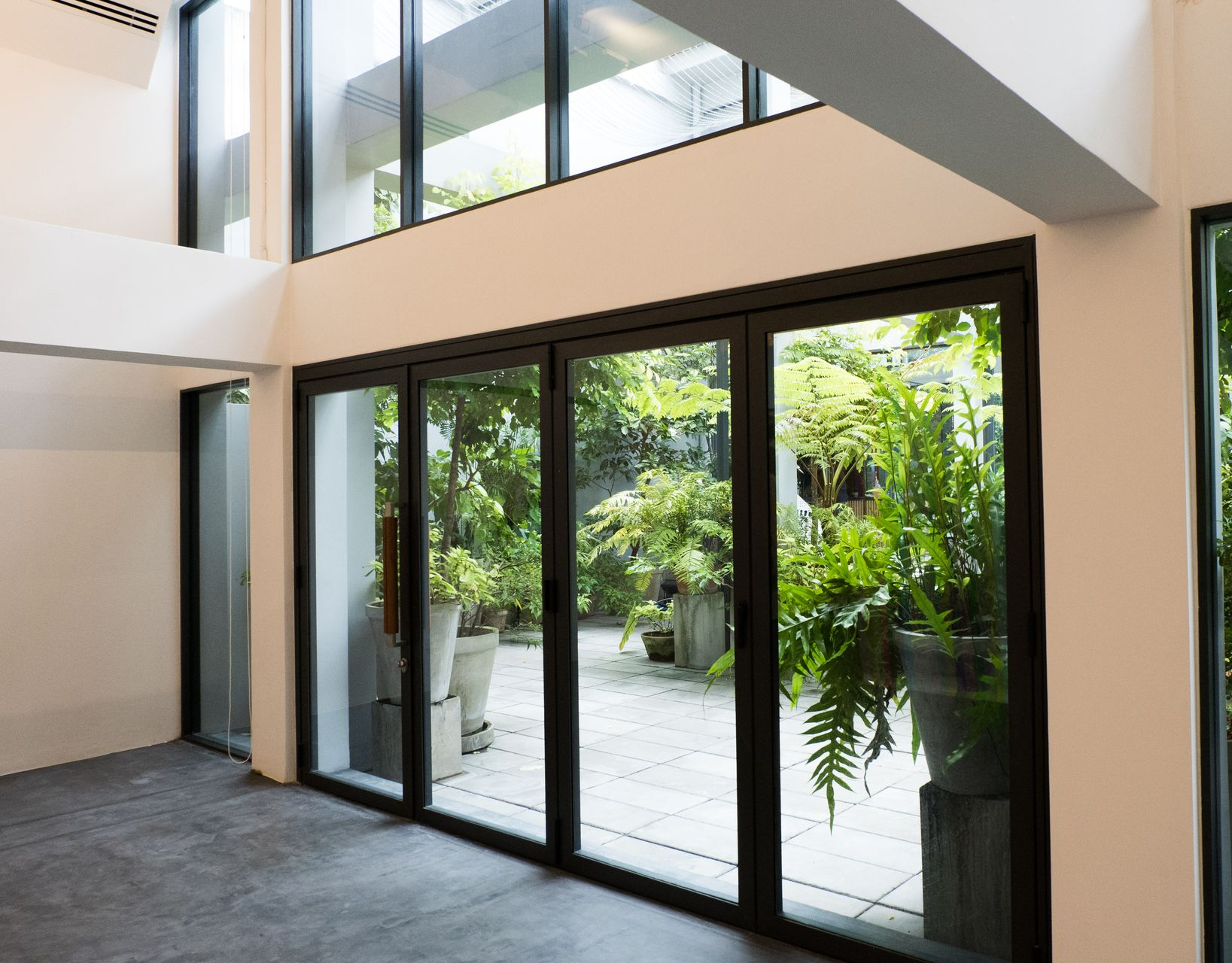 Intérieur moderne avec portes vitrées du sol au plafond et vue sur un patio avec des plantes en pot.