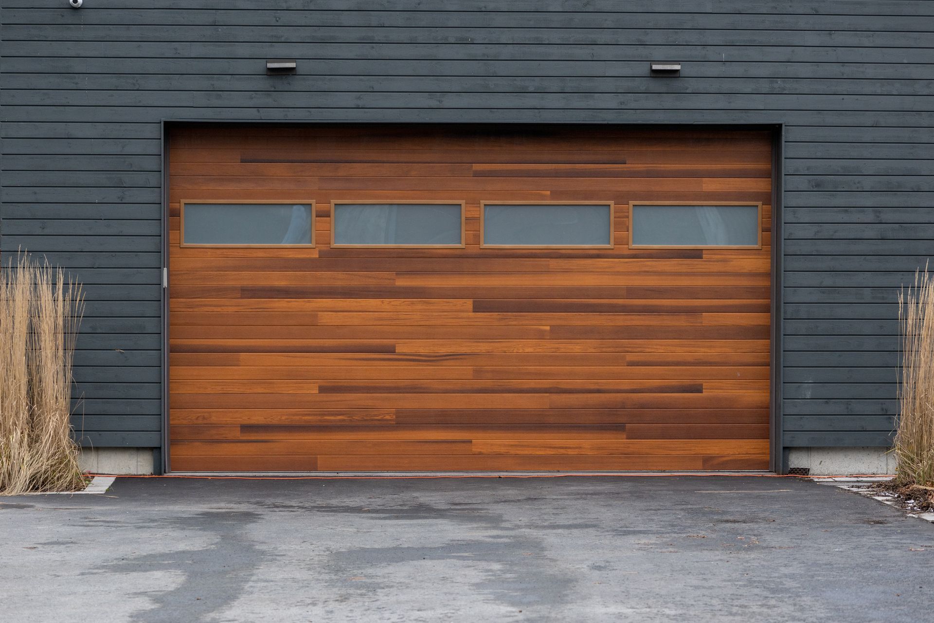 Porte de garage en bois avec quatre fenêtres rectangulaires, sur un bâtiment gris foncé.