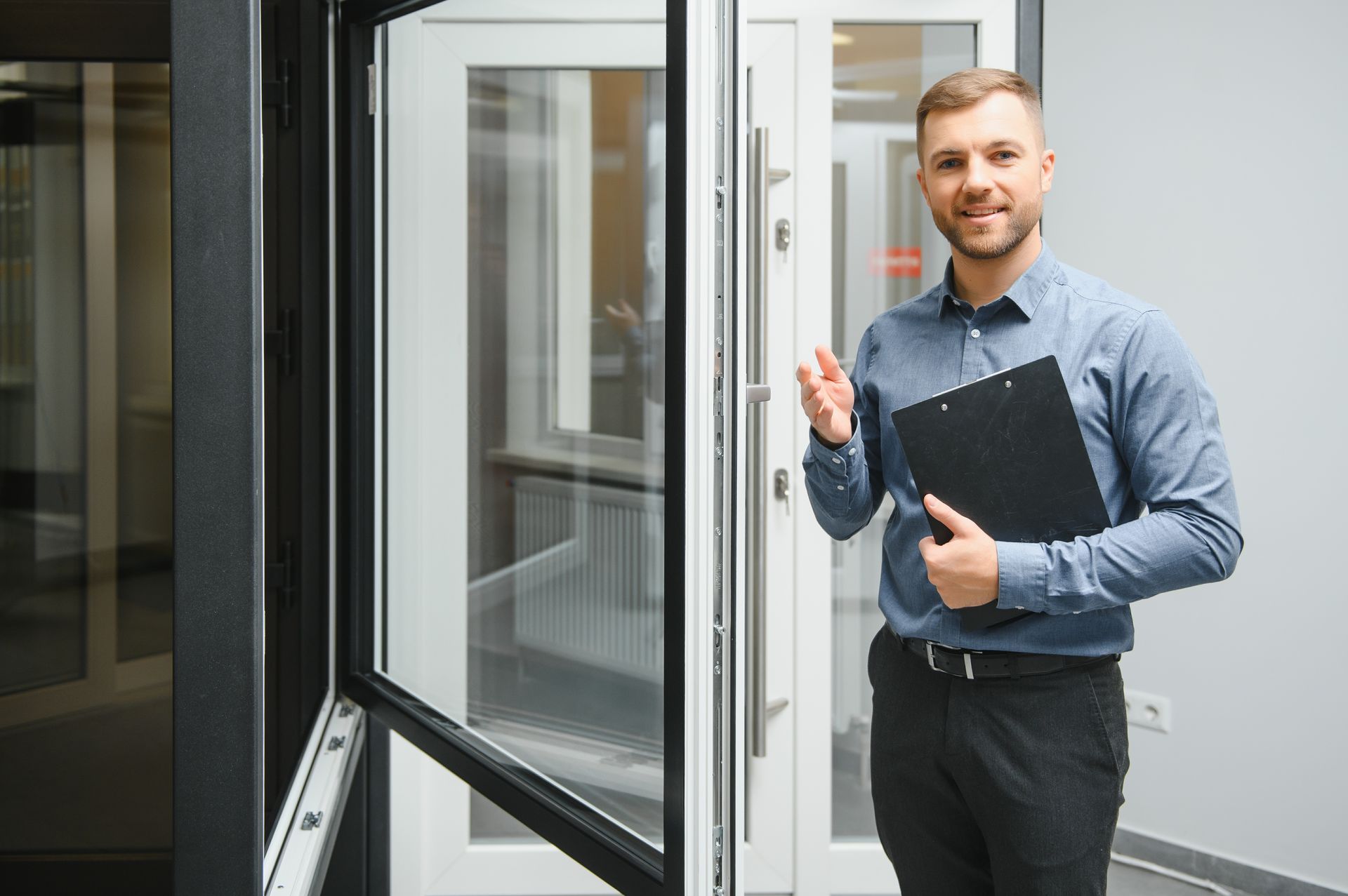Un homme en chemise bleue tient un presse-papiers et fait un geste vers une exposition de fenêtres et de portes.