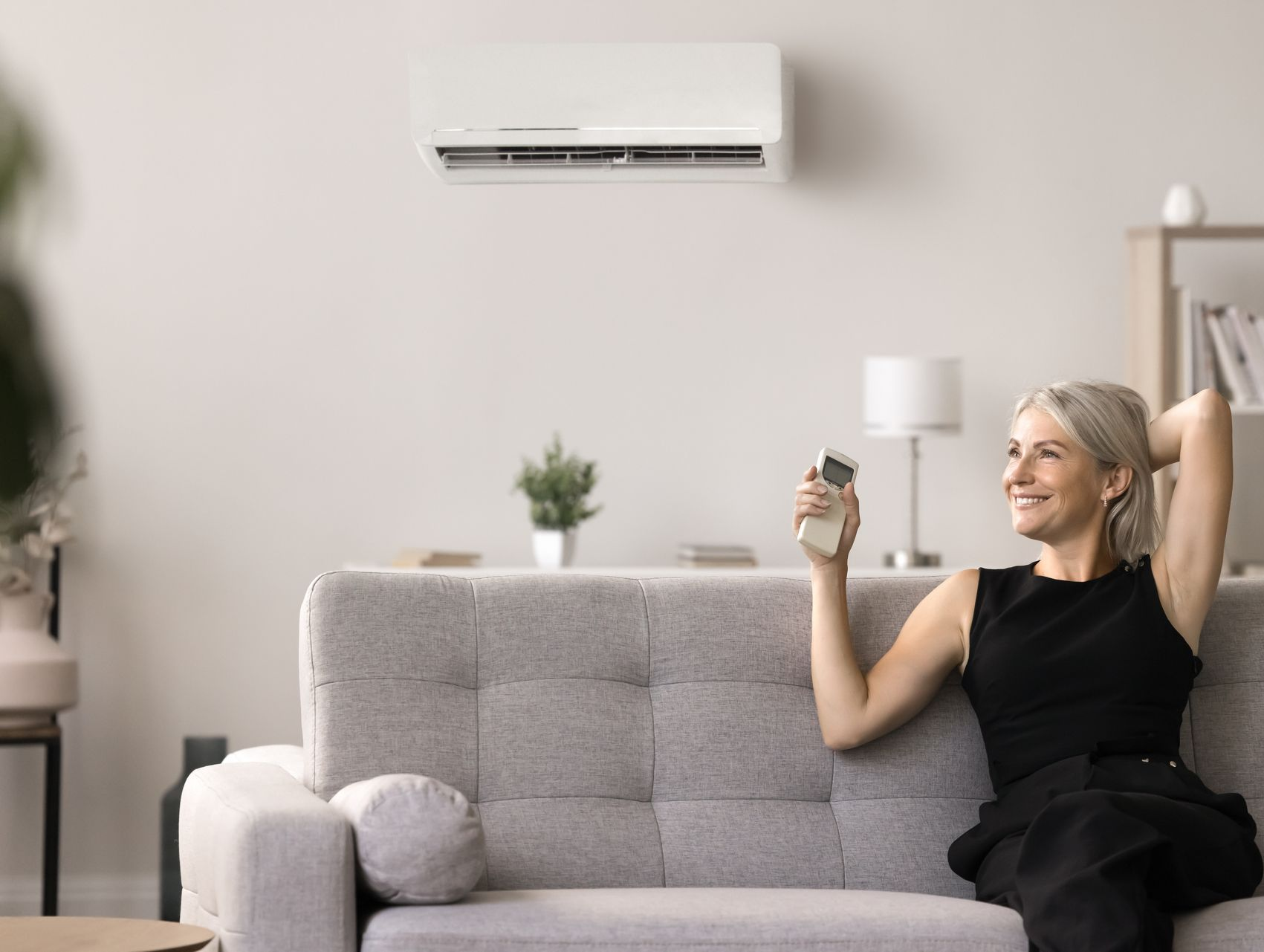Une femme se détend sur un canapé, utilisant la télécommande du climatiseur dans un salon lumineux.