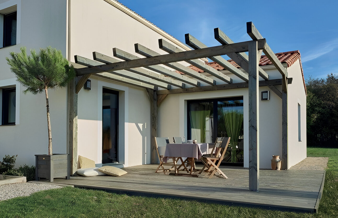 Pergola en bois au-dessus d'une salle à manger extérieure, attachée à une maison blanche avec une pelouse verte.