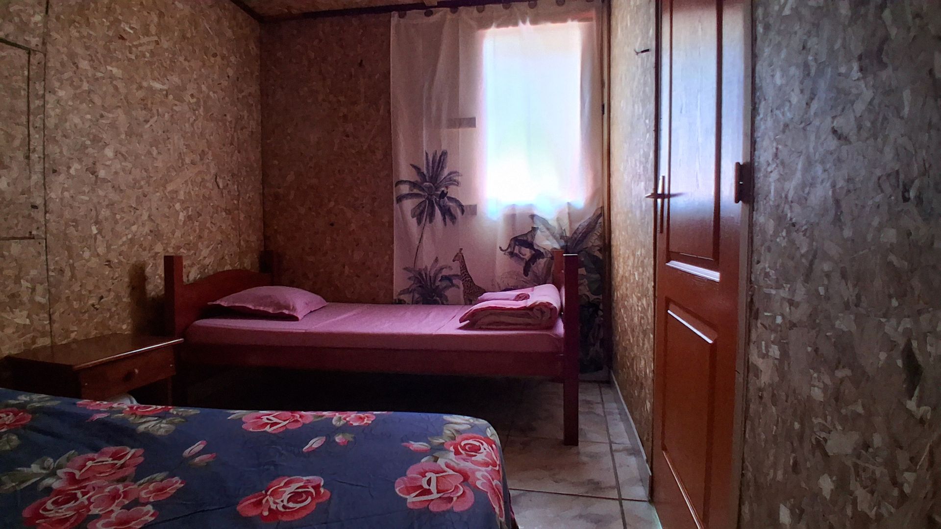 Petite chambre rustique avec deux lits, une fenêtre et une armoire en bois.