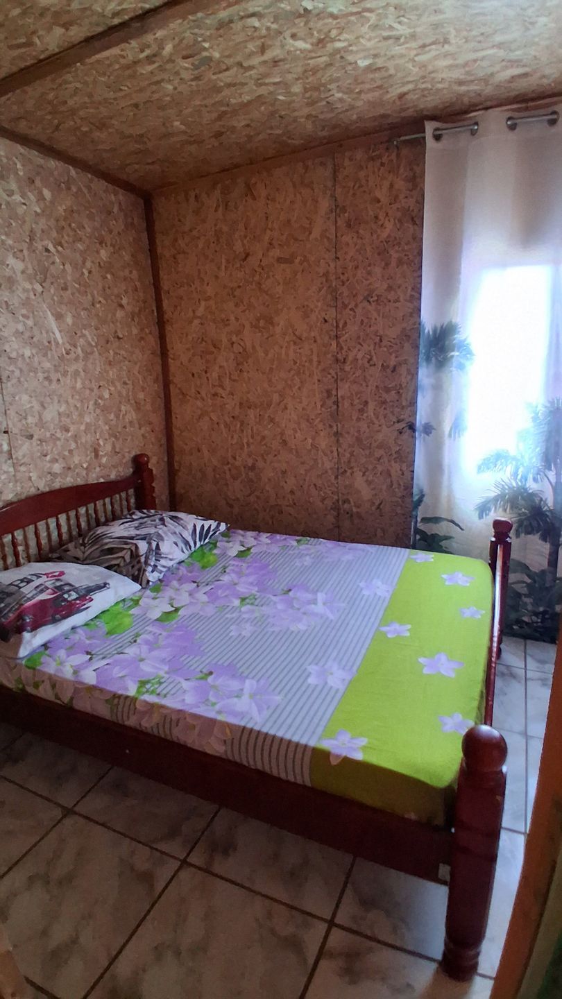 Chambre simple avec un lit en bois, un couvre-lit à fleurs et un rideau de fenêtre coloré.