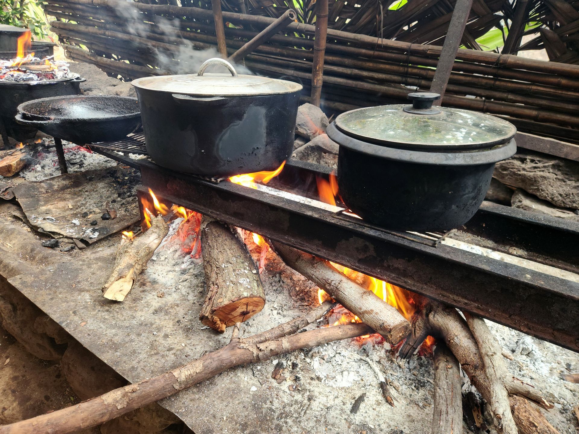 De grandes marmites mijotent sur un feu de bois ouvert, sur un poêle extérieur rustique.