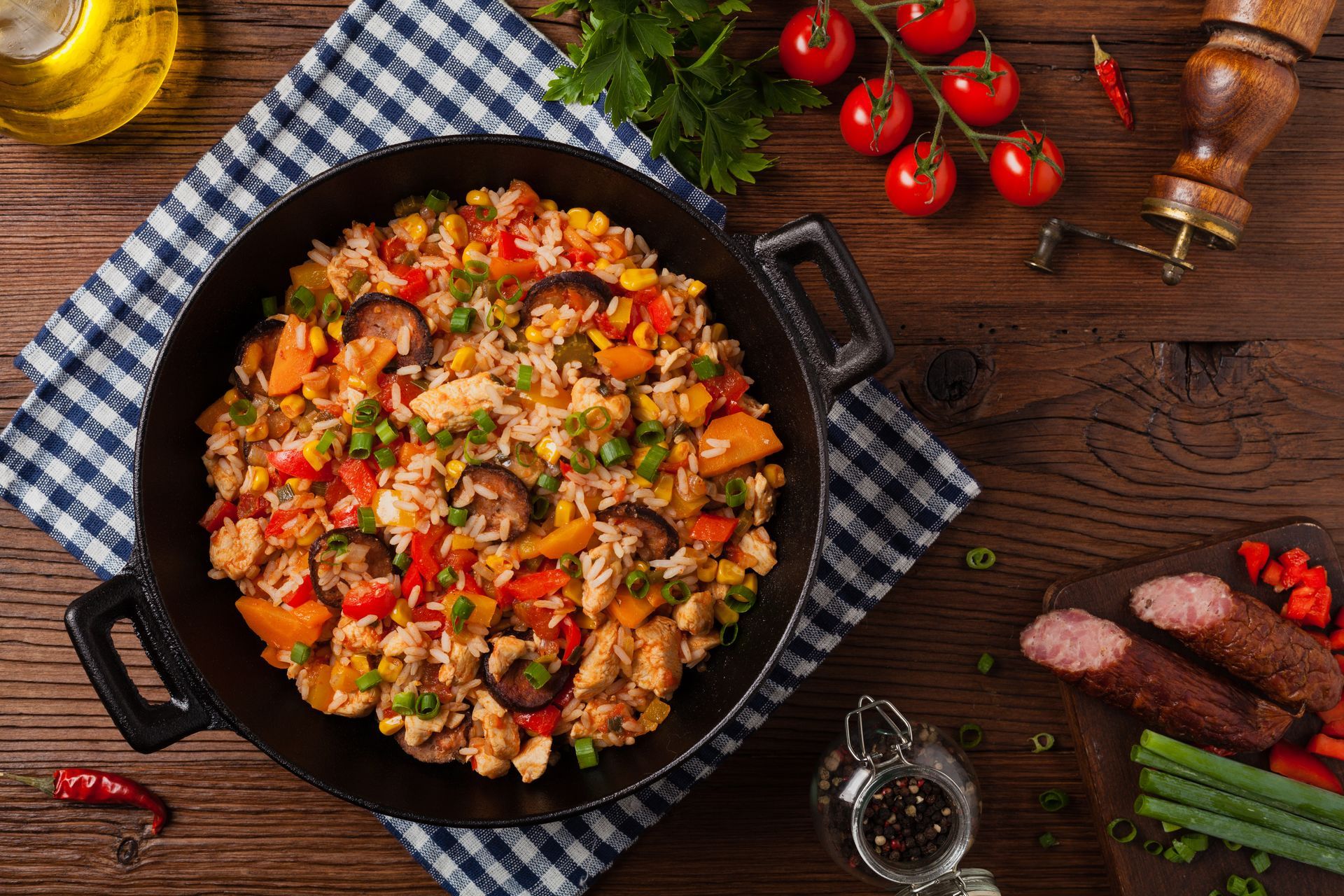 Une poêle contenant un riz sauté coloré, posée sur une table rustique en bois, avec des tomates et des herbes aromatiques.
