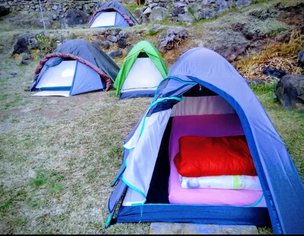 Des tentes de camping colorées sur un flanc de colline rocailleux, avec une tente bleue ouverte au premier plan.