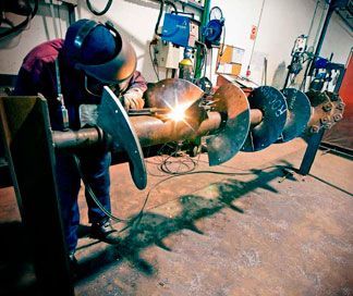 Un hombre está soldando una pieza de metal en una fábrica.