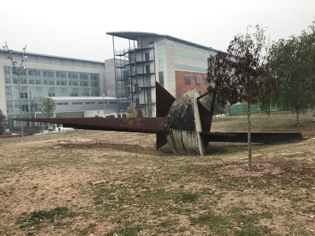 Una gran escultura se encuentra en el medio de un campo frente a un gran edificio.