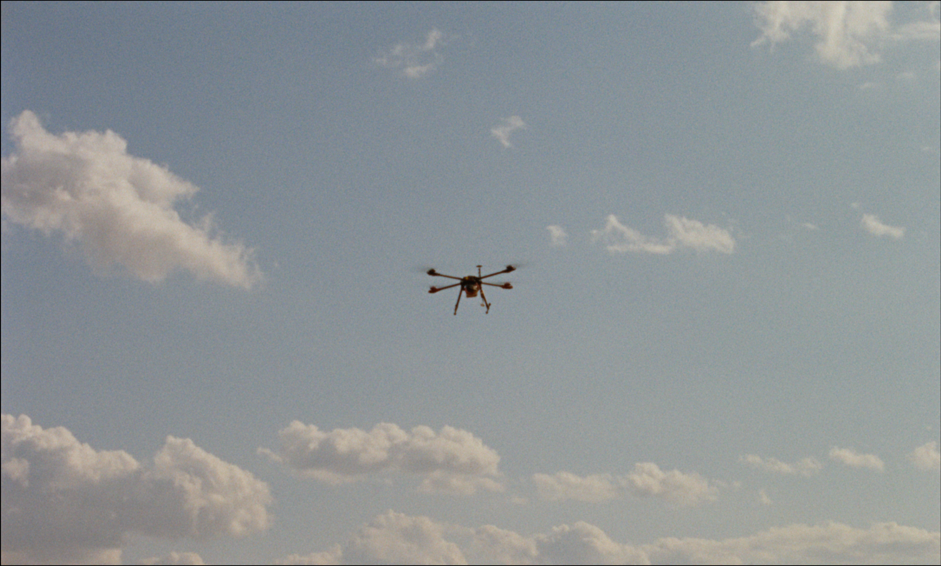 Dron volando en un cielo azul con nubes dispersas.