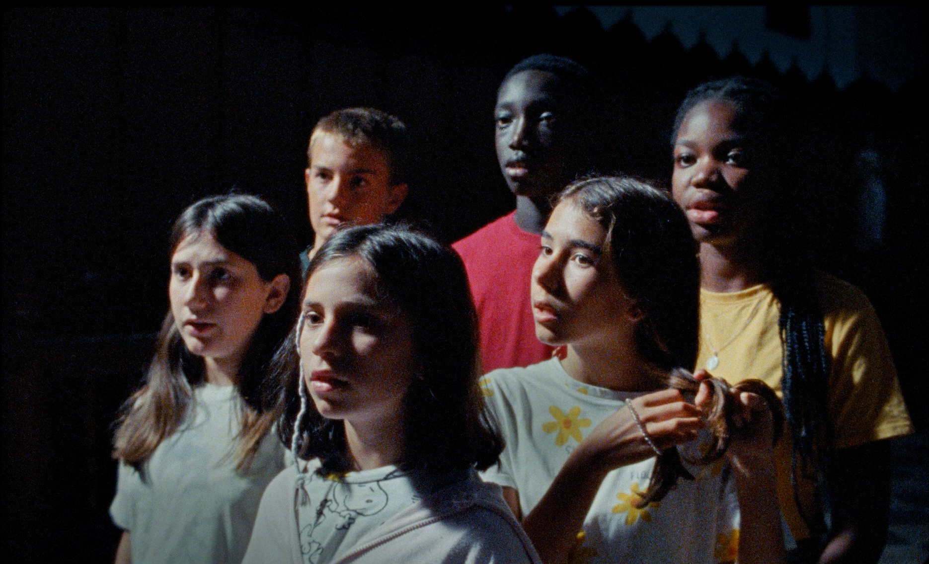 Grupo de niños mirando hacia arriba en un espacio con poca luz; sus rostros muestran sorpresa y curiosidad.