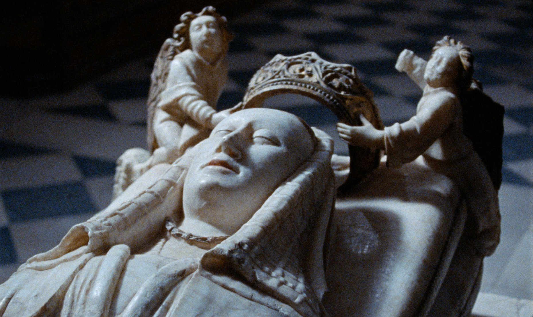 Efigie de mármol de una mujer con corona, flanqueada por ángeles, dentro de una iglesia.