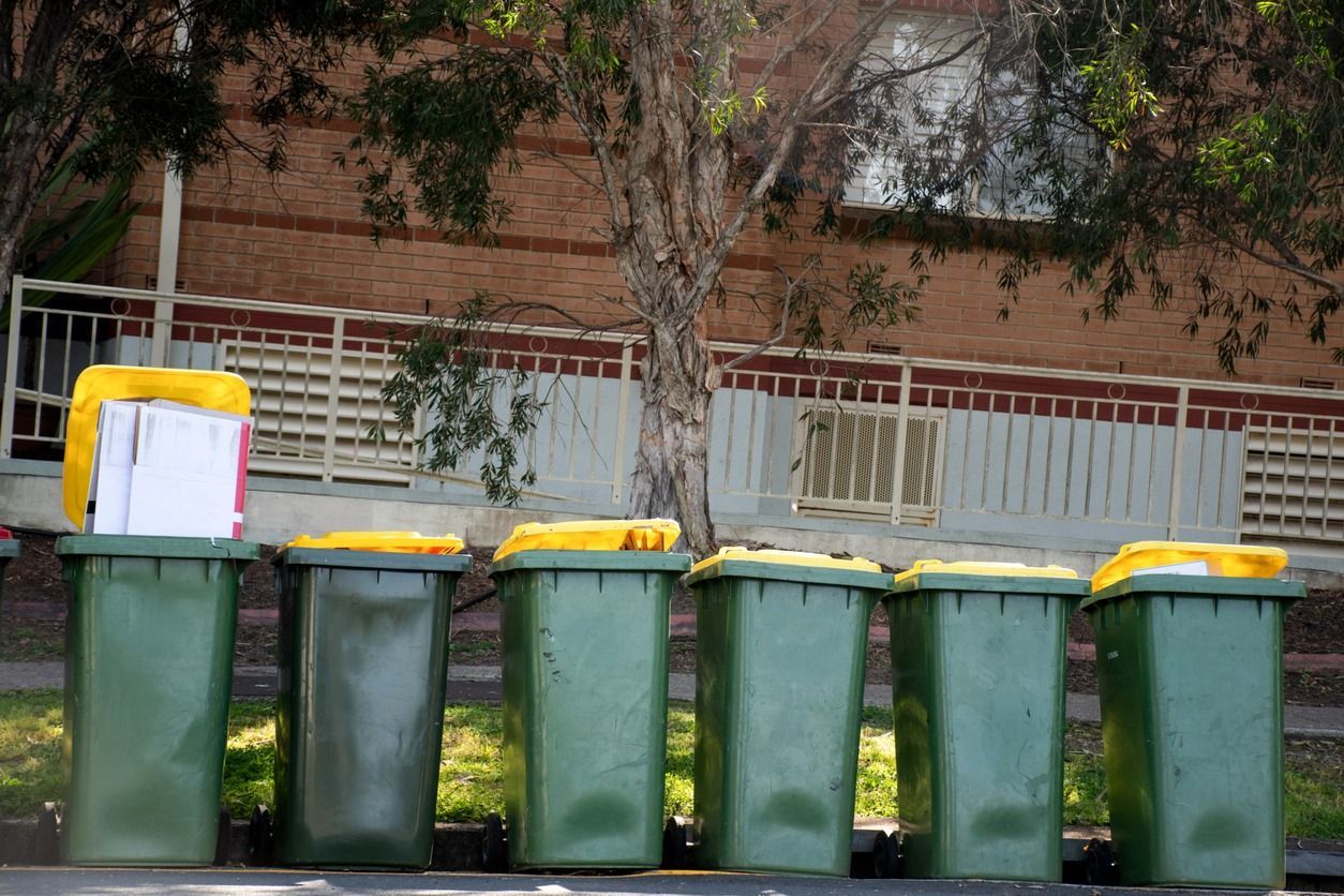 Una fila de botes de basura verdes con tapas amarillas