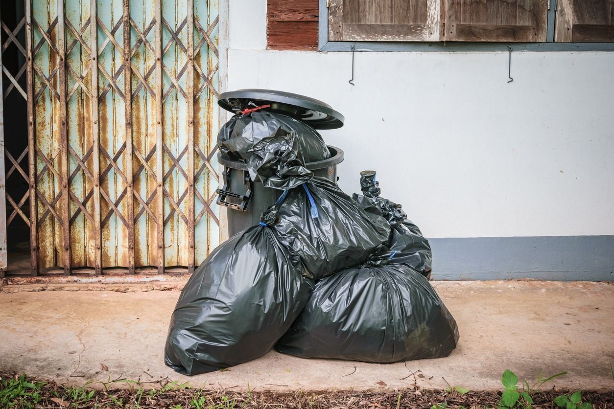 Una pila de bolsas de basura junto a un bote de basura.