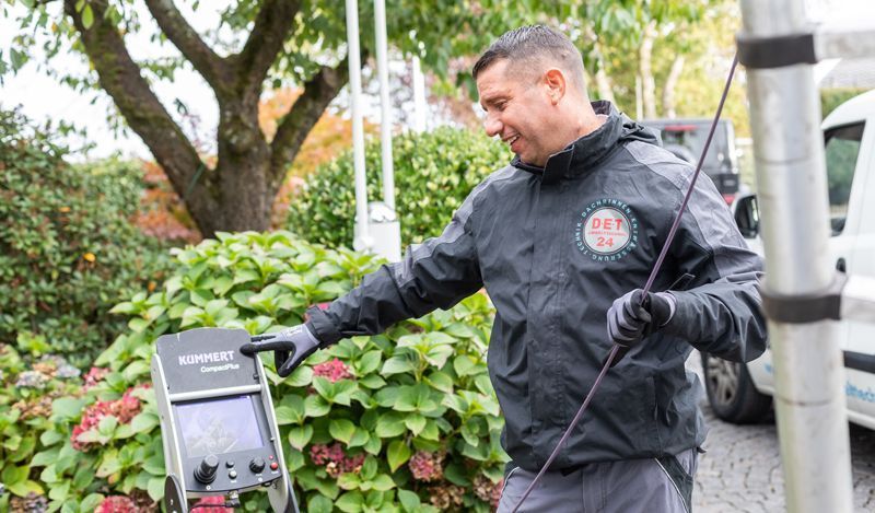 Ein Mann steht mit einem Schlauch in der Hand neben einem Baum.