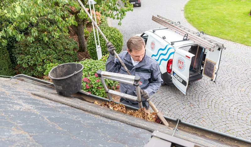 Ein Mann reinigt eine Dachrinne neben einem Lieferwagen.