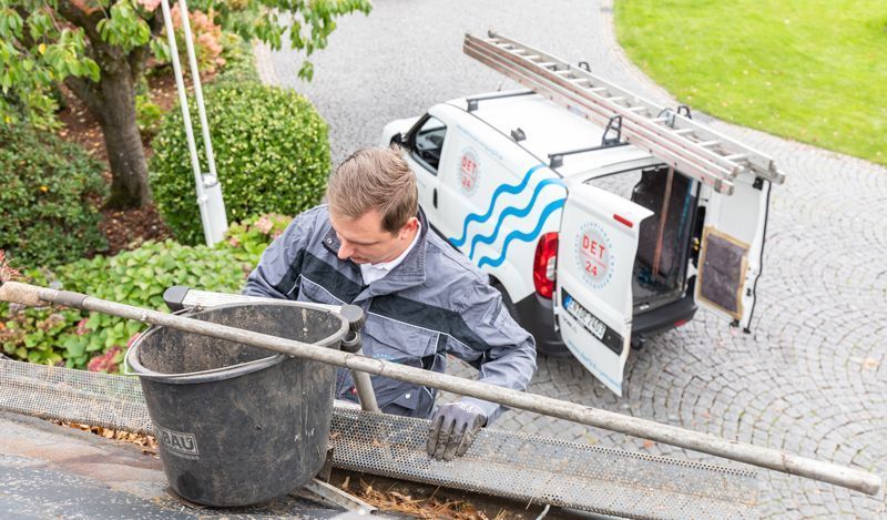 Ein Mann steht neben einem weißen Lieferwagen mit einer Leiter auf dem Dach.