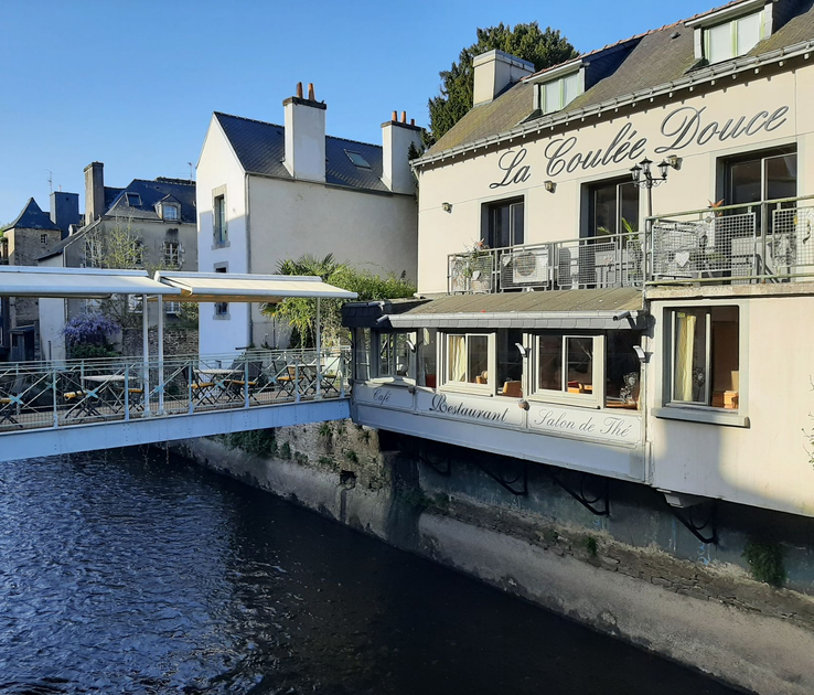 Un restaurant nommé La Coulée Douce  avec une terrasse extérieure donnant sur un canal dans une ville historique européenne.